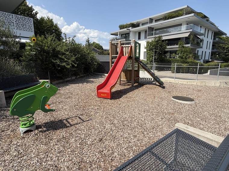 Aire de jeux avec toboggan rouge et jeu à ressort sur sol en copeaux de bois
