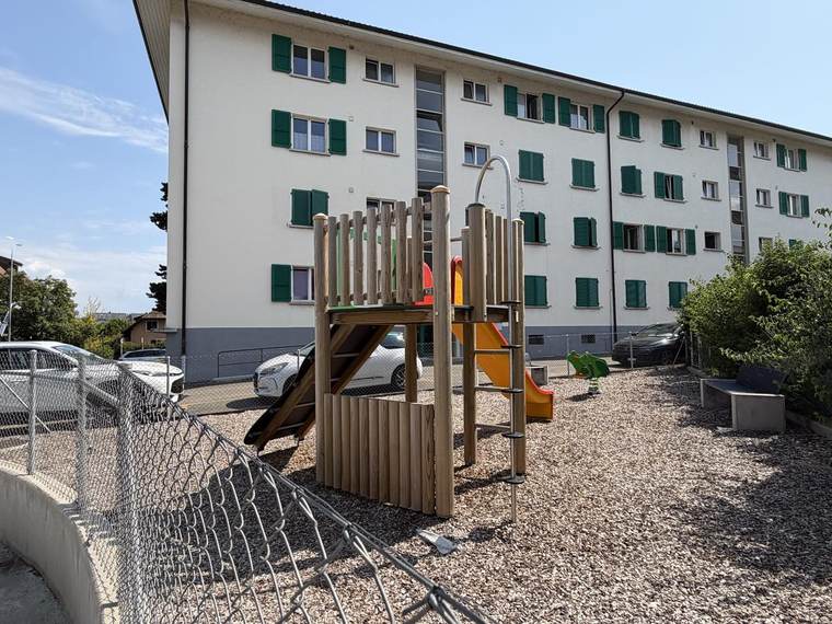 Tour de jeu en bois avec toboggan et échelle, devant un immeuble résidentiel